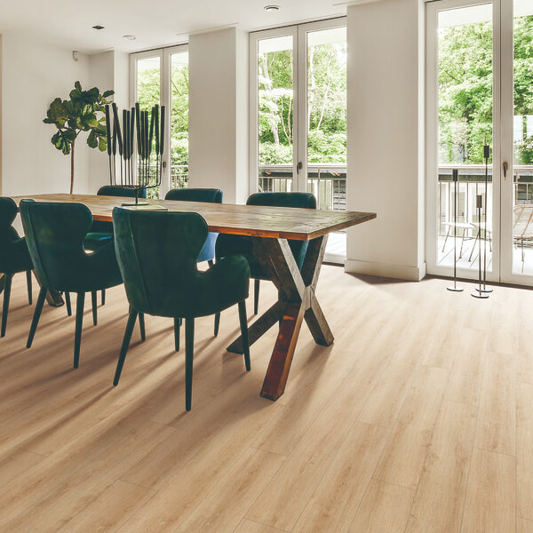 Salón comedor amplio de concepto abierto con suelo SPC Sakura Almond de TRIP The Natural Company, gran mesa de madera, sillas velvet verde esmeralda y ventanales al jardín.