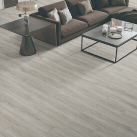 Salón de diseño con suelo de gran formato SPC Cerato Abedul de TRIP The Natural Company, sofá curvo marrón chocolate, mesitas de centro minimalistas oscuras y suelo gris claro.