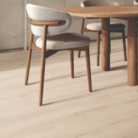 Comedor de diseño orgánico con suelo de SPC Merisier Bone de TRIP The Natural Company, mesa de madera, sillas tapizadas y hornacina de piedra texturizada en el fondo.