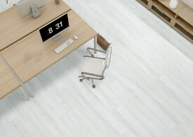 Despacho de oficina visto desde arriba con suelo SPC Sakura Gris de TRIP The Natural Company, escritorio de madera clara, ordenador, silla de diseño y mueble bajo.